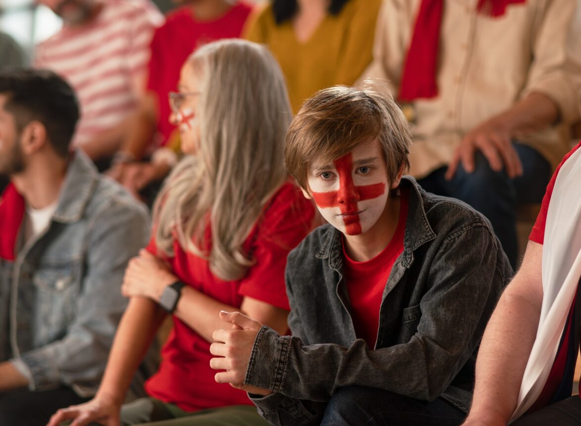 Excited football fans supporting English national team in live soccer match at stadium.