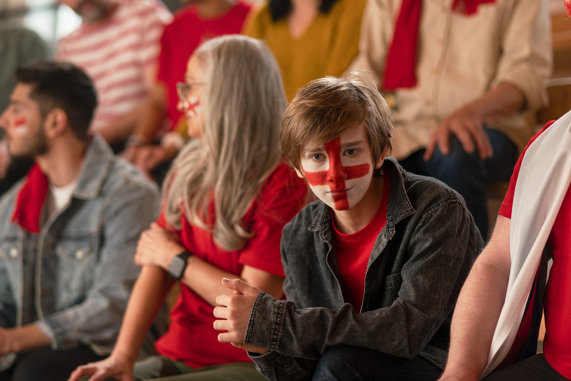 Excited football fans supporting English national team in live soccer match at stadium.