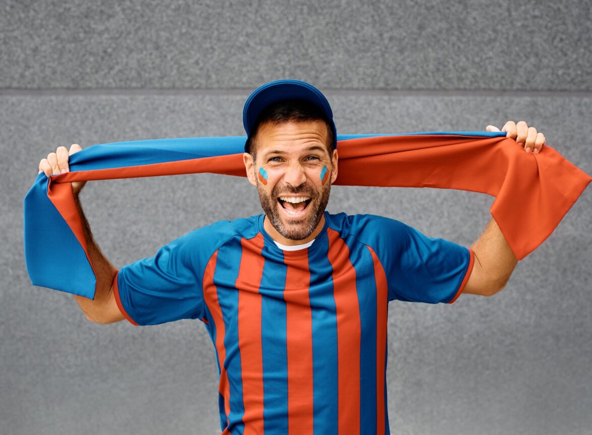 Excited man in soccer jersey shouting while cheering and looking at camera.