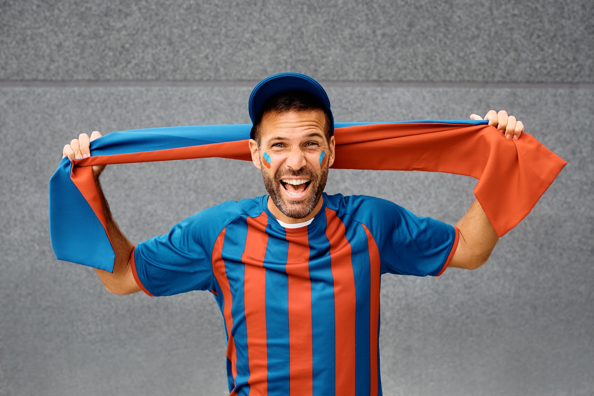 Excited man in soccer jersey shouting while cheering and looking at camera.